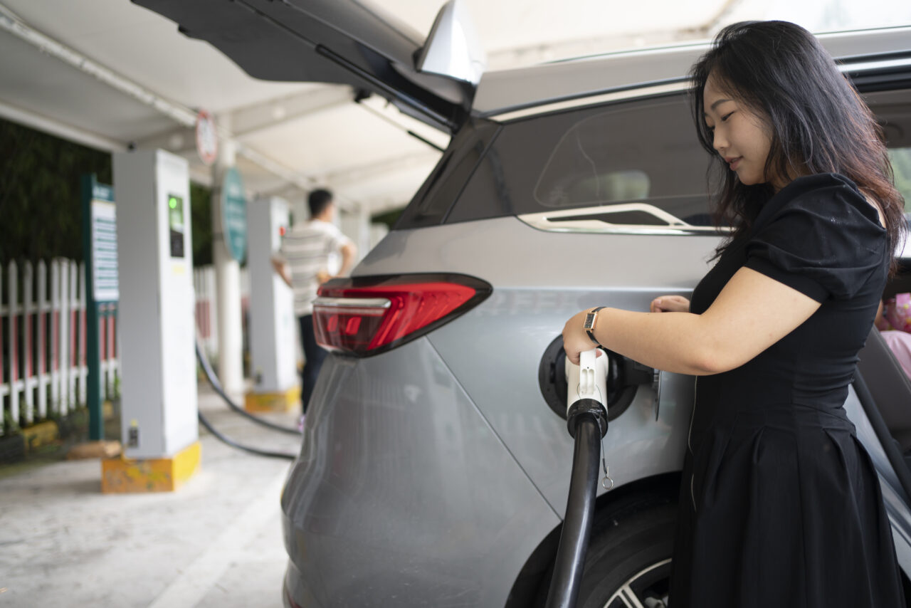 Woman Plugging Electric Vehicle Into Charger at Station